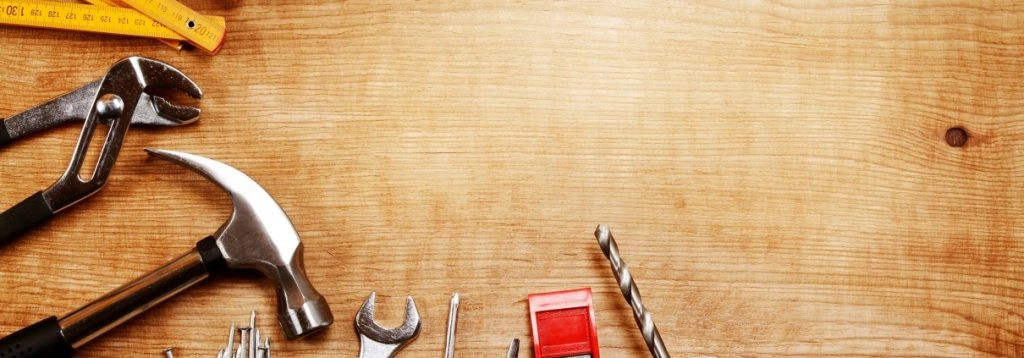 A collection of essential home improvement tools on a wooden surface, including a hammer, pliers, and a drill.
