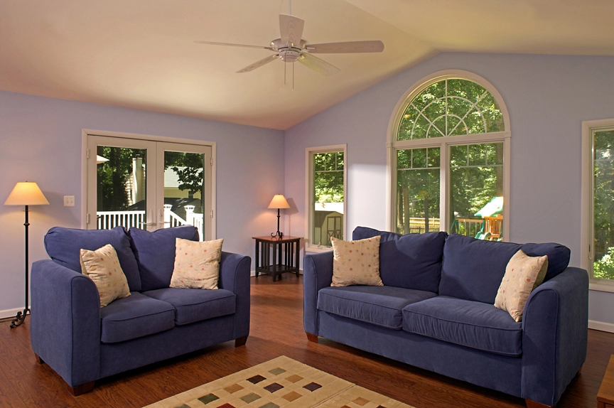 Cozy living room featuring blue sofas, wooden flooring, and large windows letting in natural light.