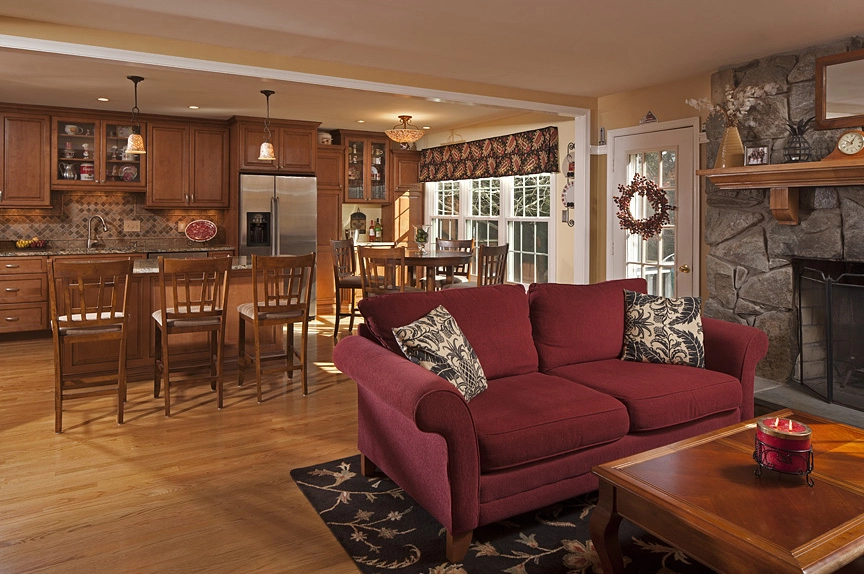 Cozy living room with a burgundy sofa, wooden dining area, and modern kitchen features in a remodeled home.