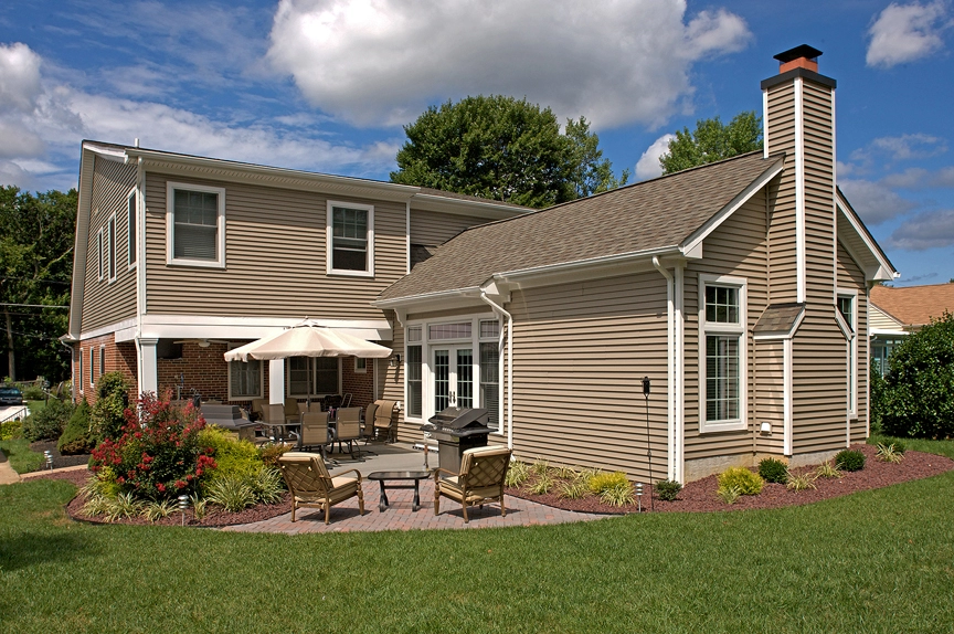 A beautifully remodeled home exterior featuring tan vinyl siding and a cozy patio with seating.