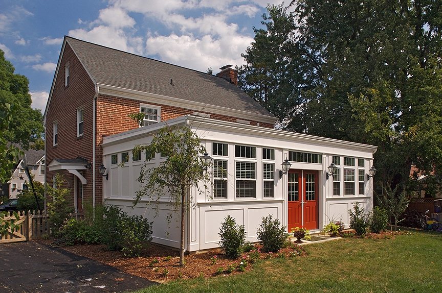 Bright white sunroom addition with large windows and red double doors, surrounded by green landscaping in Catonsville.