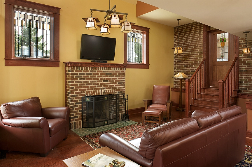 Cozy living room featuring leather chairs, brick fireplace, and warm yellow walls in a remodeled home.