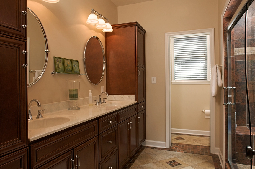 Modern bathroom featuring a double vanity with dark wood cabinets, round mirrors, and a glass shower enclosure.