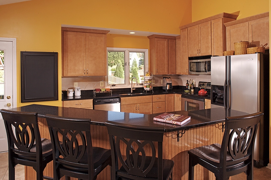 Bright kitchen featuring wooden cabinets, black countertops, and stainless steel appliances, ideal for modern homes.