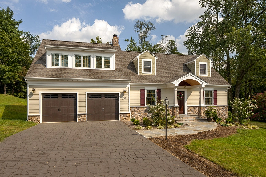 Charming residential home featuring a light-colored facade, dual garage doors, and landscaped surroundings.