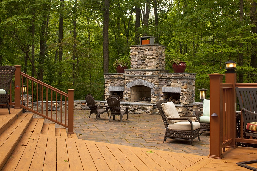 Outdoor living space featuring a stone fireplace surrounded by comfortable seating and lush greenery.