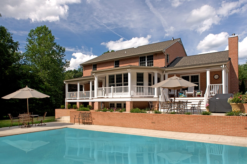 Spacious backyard featuring a blue swimming pool and a brick house with a large porch and outdoor seating.