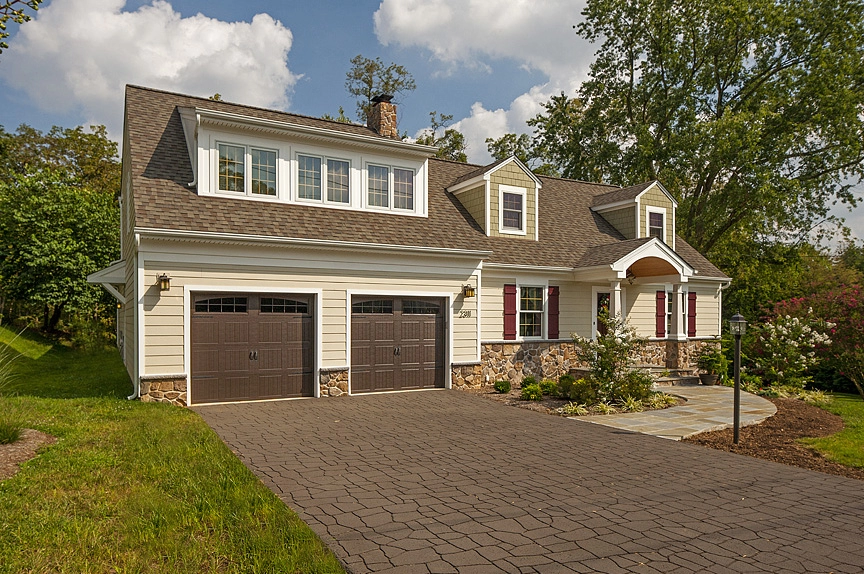 Charming suburban home featuring a light-colored exterior, stone accents, and a paved driveway.