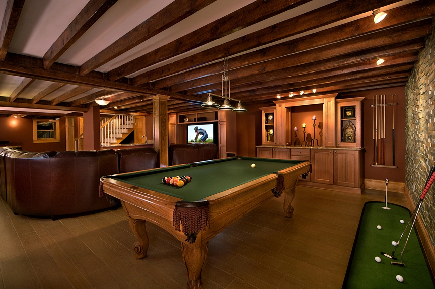 Luxurious basement game room featuring a green pool table, cozy leather seating, and elegant wood accents.