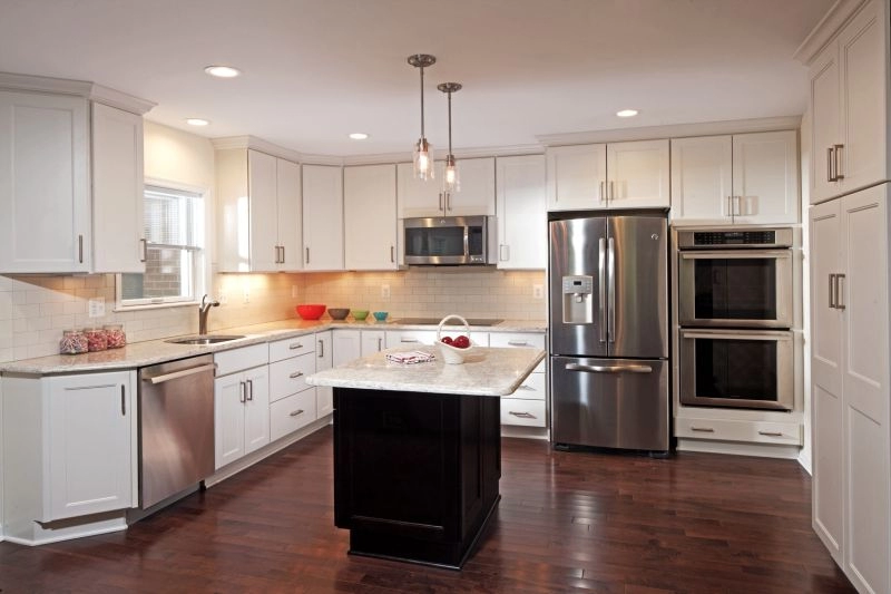 Modern kitchen featuring white cabinetry, stainless steel appliances, and a dark kitchen island with marble countertop.