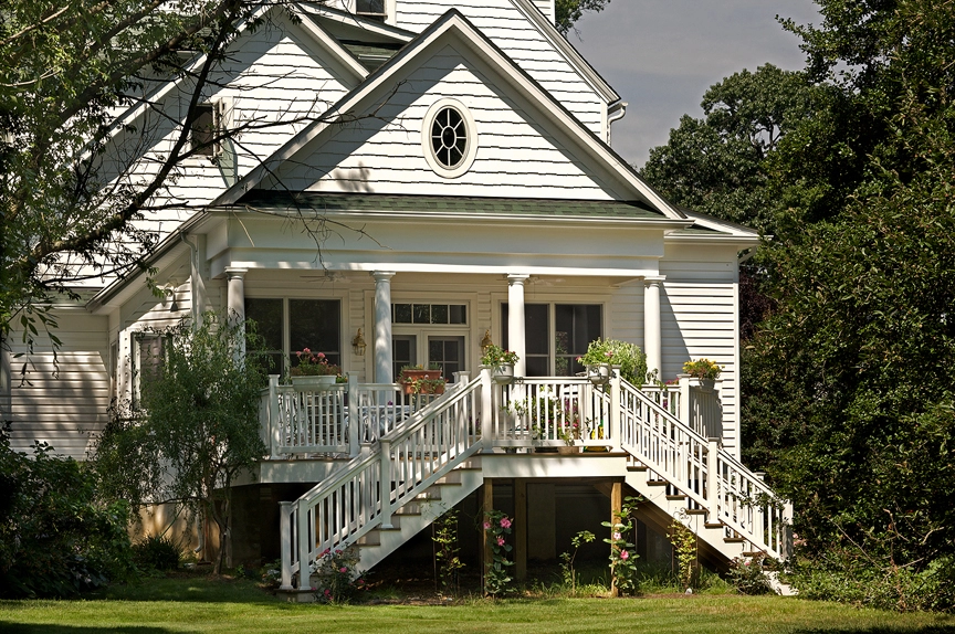 Charming white house with a porch, featuring stairs and lush greenery surrounding it, ideal for roofing and siding projects.
