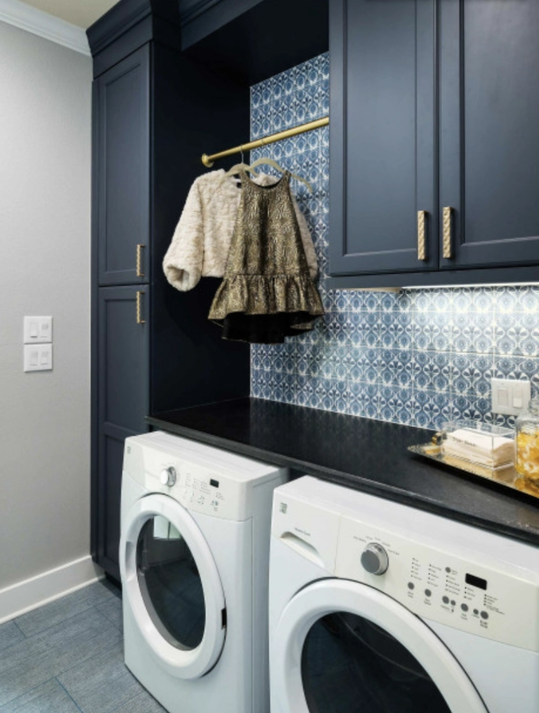 Stylish laundry room featuring white washer and dryer, navy cabinets, and patterned blue backsplash.