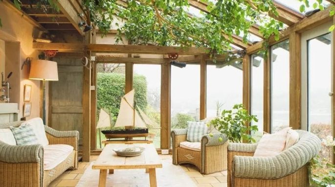 Bright sunroom with glass roof, wooden beams, and cozy wicker furniture, ideal for house additions.