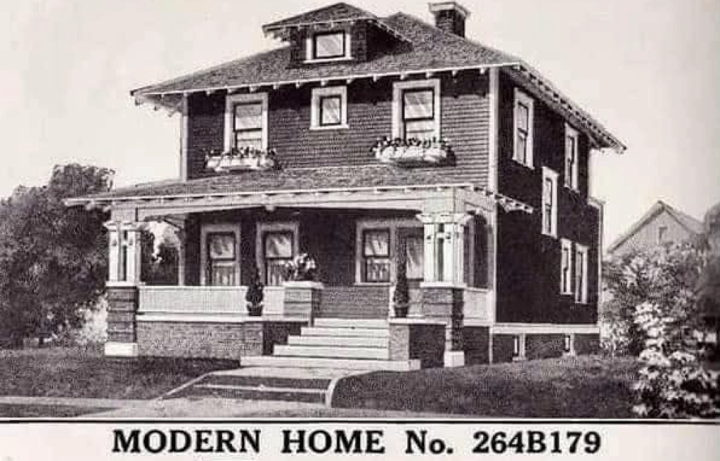 Two-story Sears home featuring a wide porch, decorative gables, and large windows, showcasing classic American architecture.
