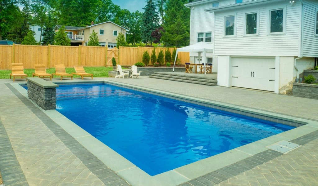 Sparkling blue swimming pool surrounded by stone patio and lounge chairs, perfect for outdoor relaxation.