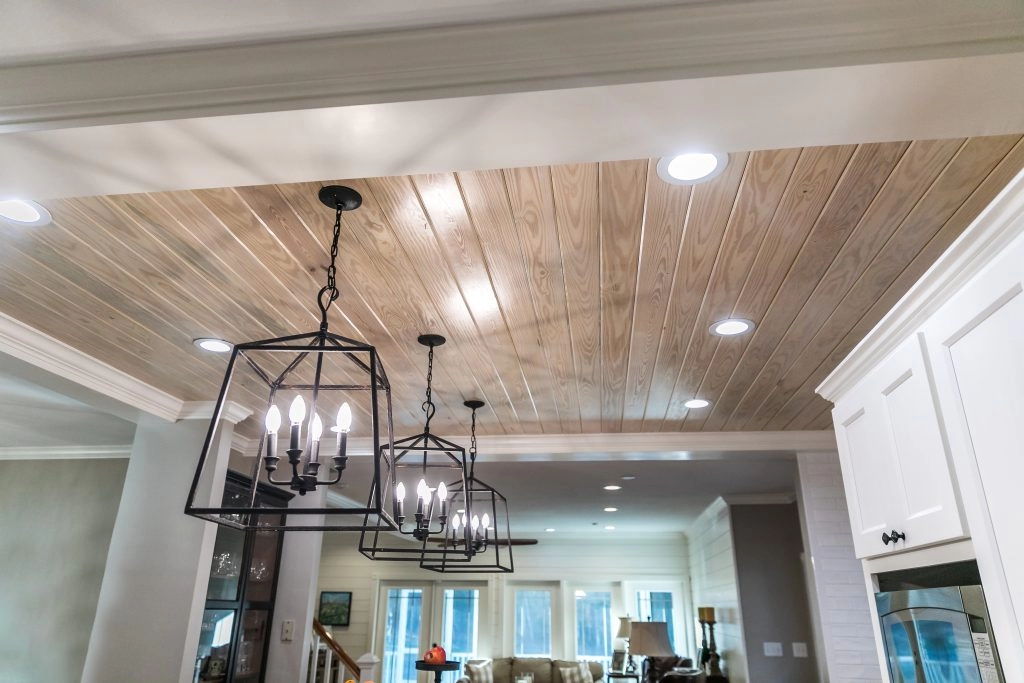 Stylish black metal pendant lights hang from a wooden ceiling in a renovated kitchen, enhancing its modern aesthetic.