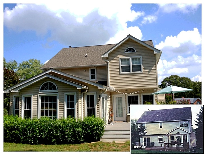 Two-story beige house with front porch and large windows, featuring a remodeled roof and landscaping.